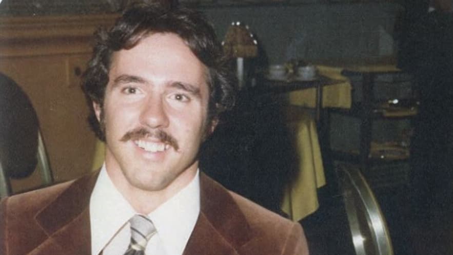 Ric Weiland with a mustache, smiling. The top of his brown suit showing.