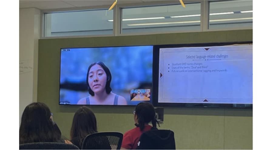 An audience looks on at a large screen monitor as Amari Pierce speaks to them virtually.