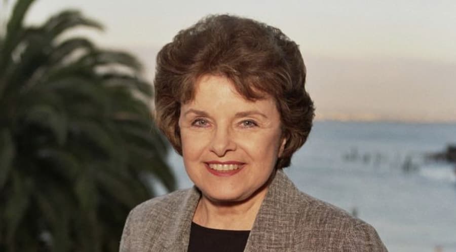 Dianne Feinstein standing in front of a waterfront at sunset smiling at the camera.
