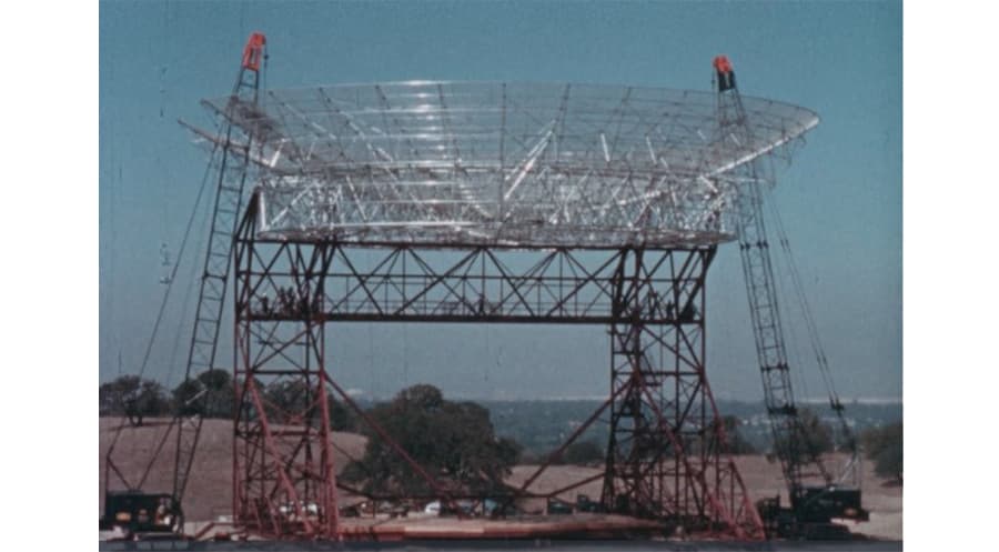 A large radio anntena flanked by two construction cranes.