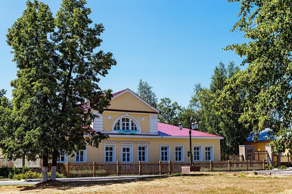 Yellow single story house with an attic and a wooden picket fence in front.